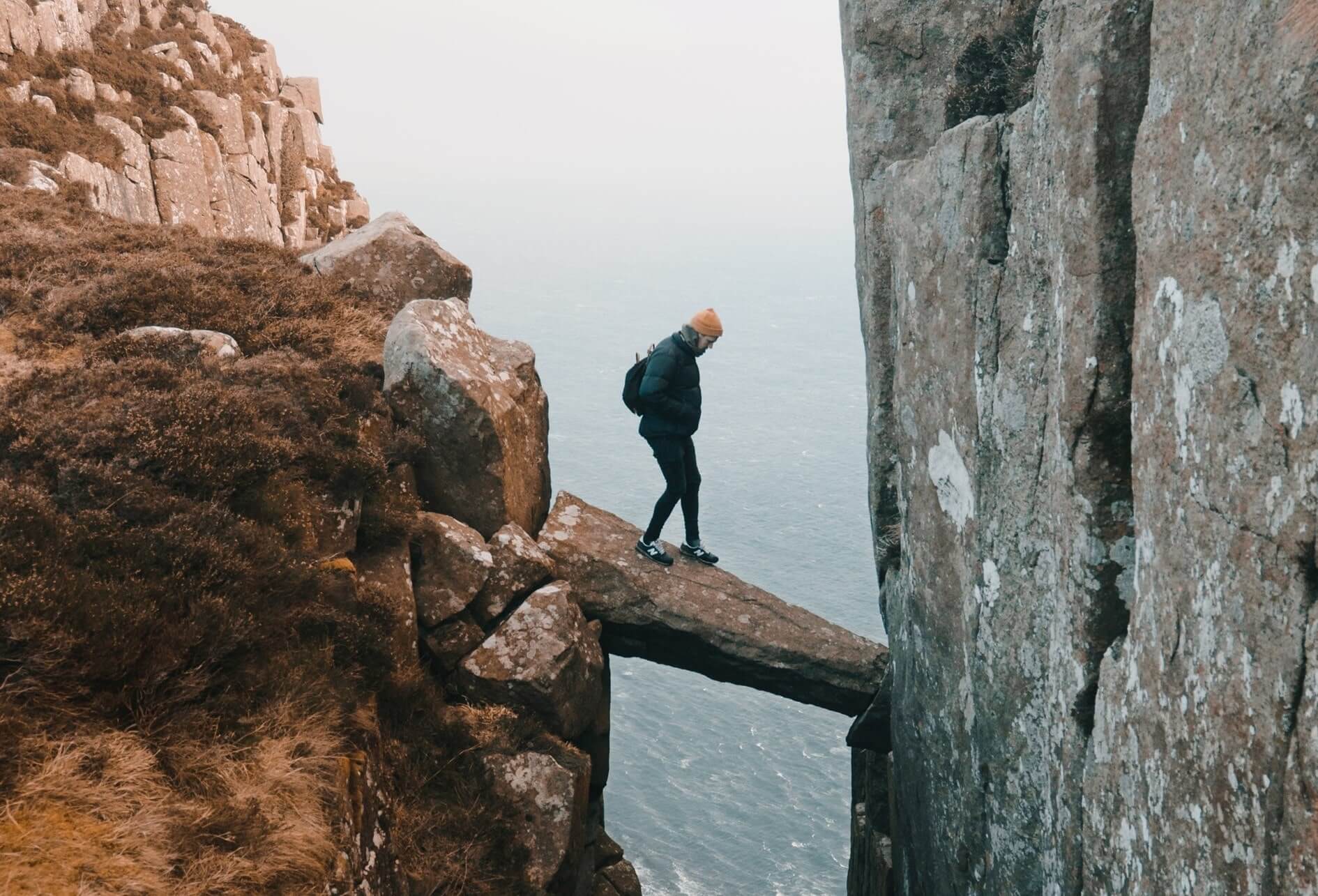 Humain sur une roche en équilibre précaire au-dessus d’un précipice et deux falaises