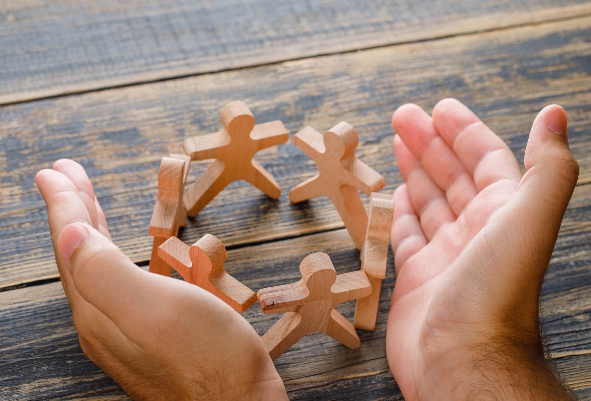 Sur une table, un cercle de figurines humaines en bois protéger par des mains