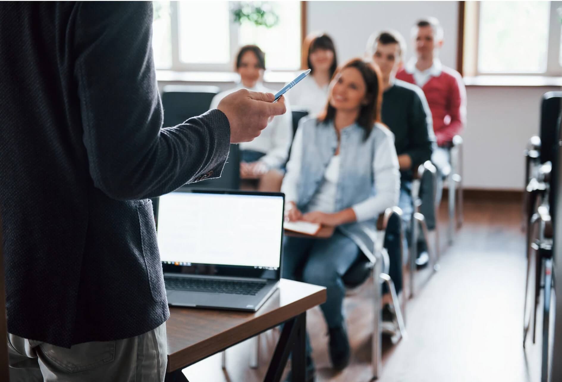 Formation instruction Au premier plan le formateur, en arrière-plan flou, les élèves dans une classe.