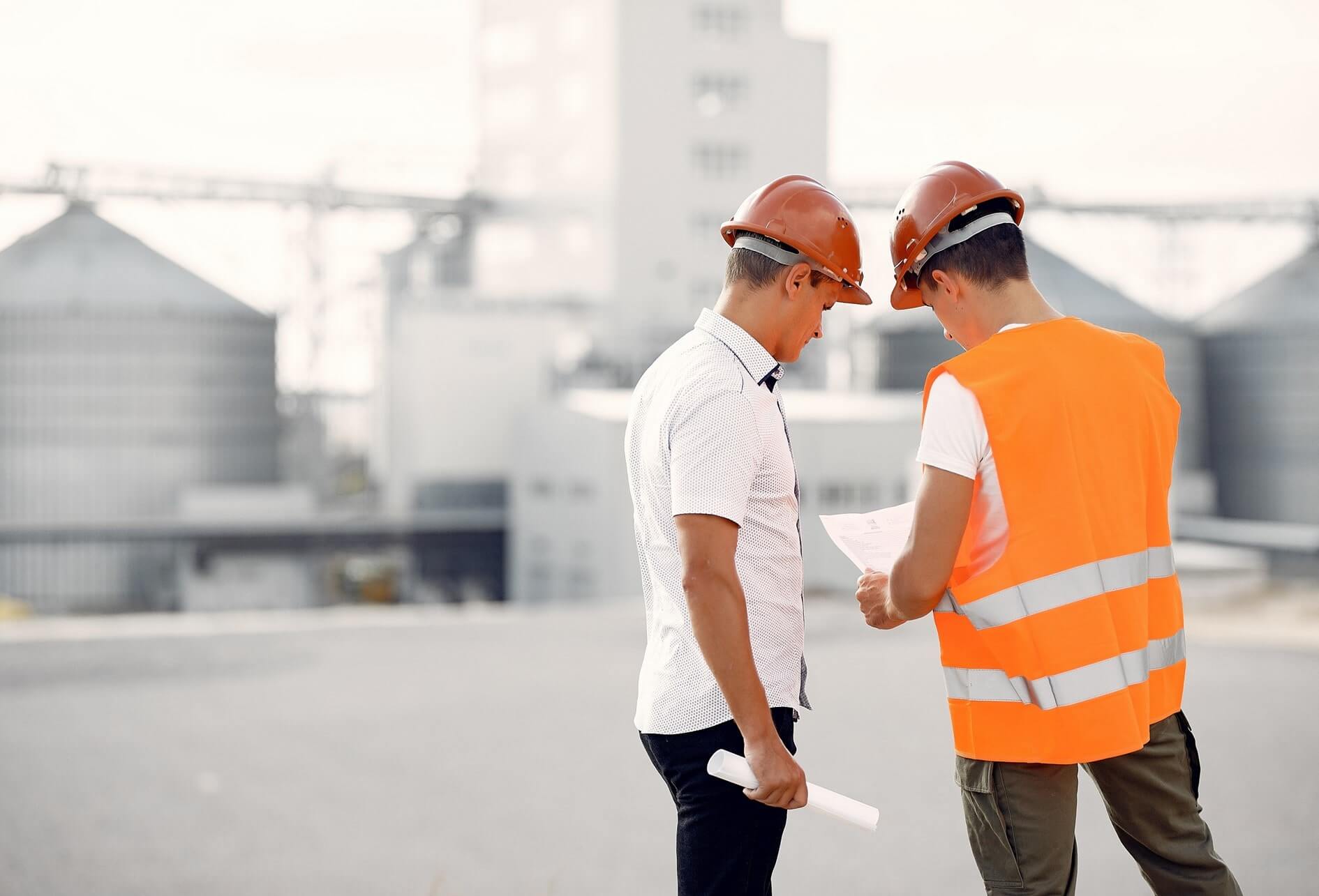 Deux techniciens casqués réalisant une étude technique de plan sur un arrière-plan flou d’usine